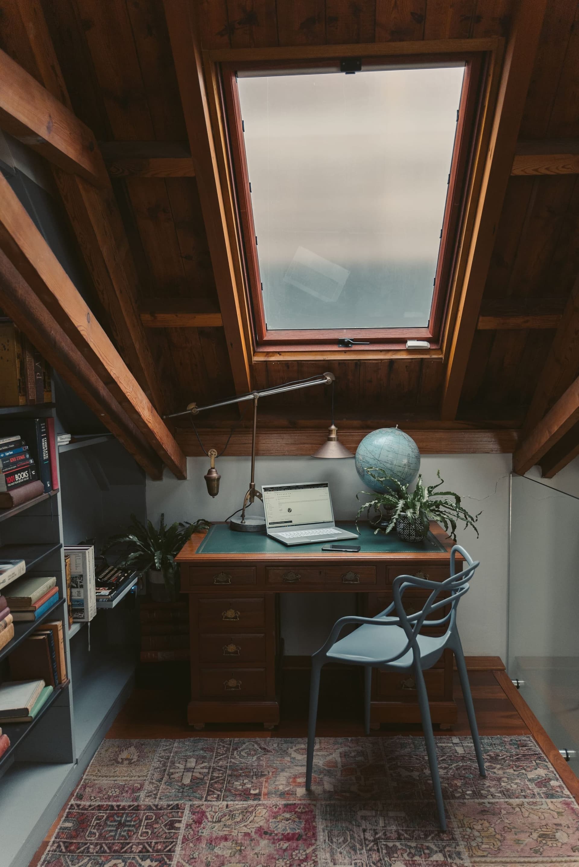 Study under a sloping ceiling with a roof window above the desk and shelves of books