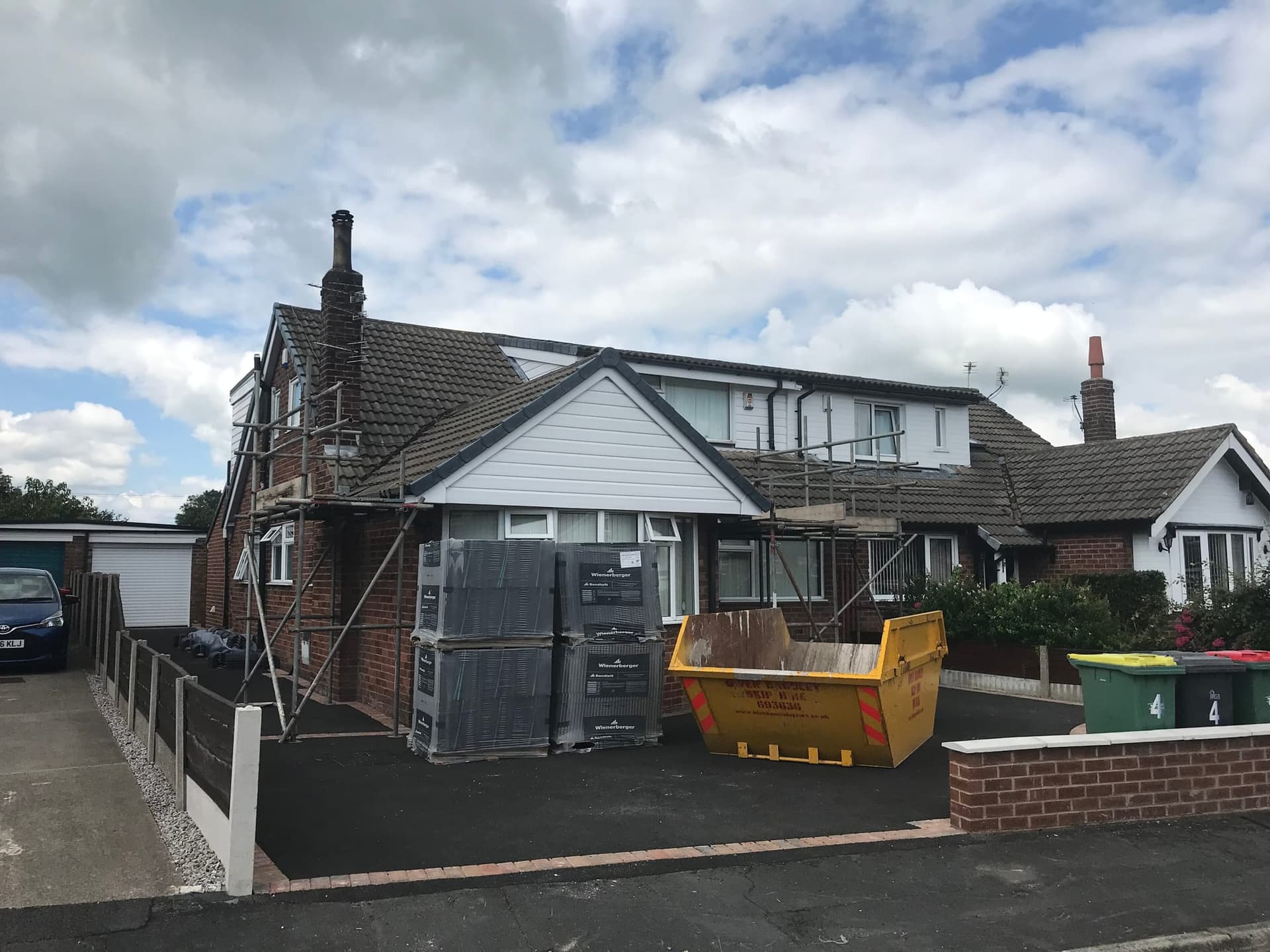 A bungalow with a new front dormer under construction, roof tiles stacked on the drive and a skip outside