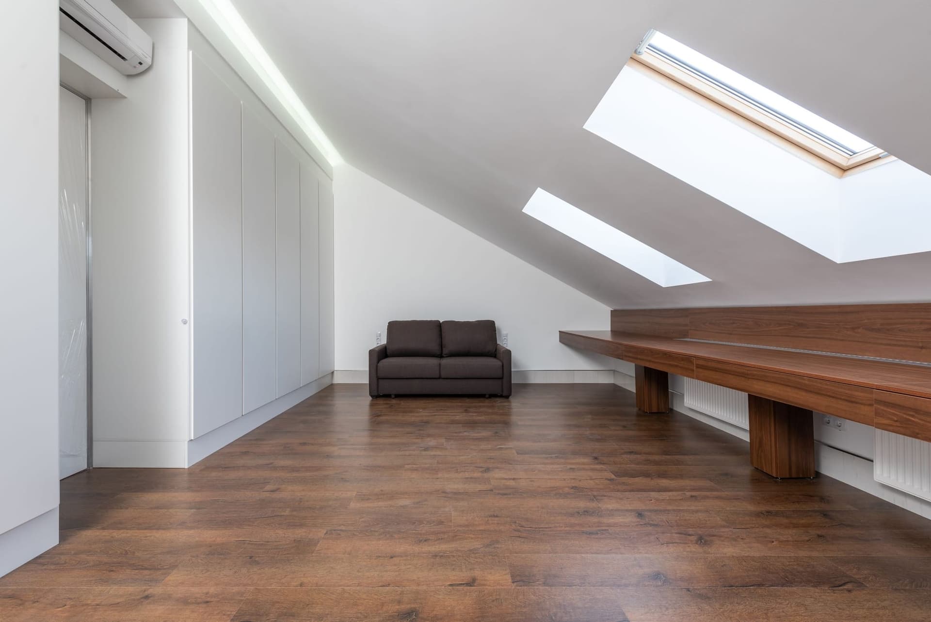Empty loft room with three rooflights, a timber window seat and fitted storage under the eaves