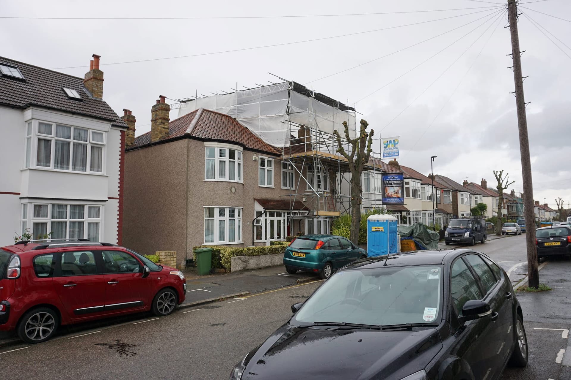A semi-detached house on Dallinger Road wrapped in scaffolding for a loft conversion, beside its unconverted neighbours