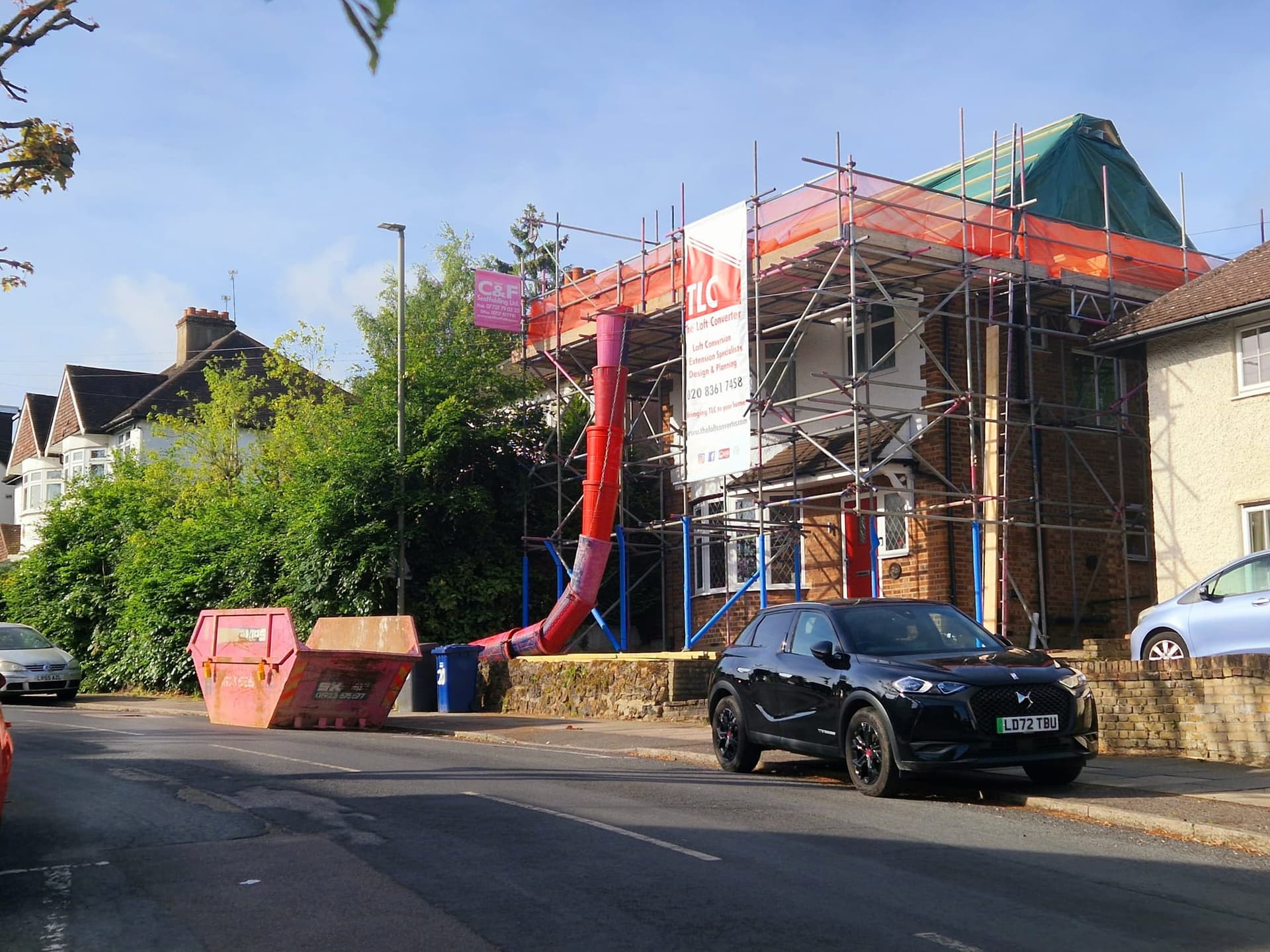 A house in East Barnet under scaffolding for a loft conversion, with a rubble chute running down into a skip