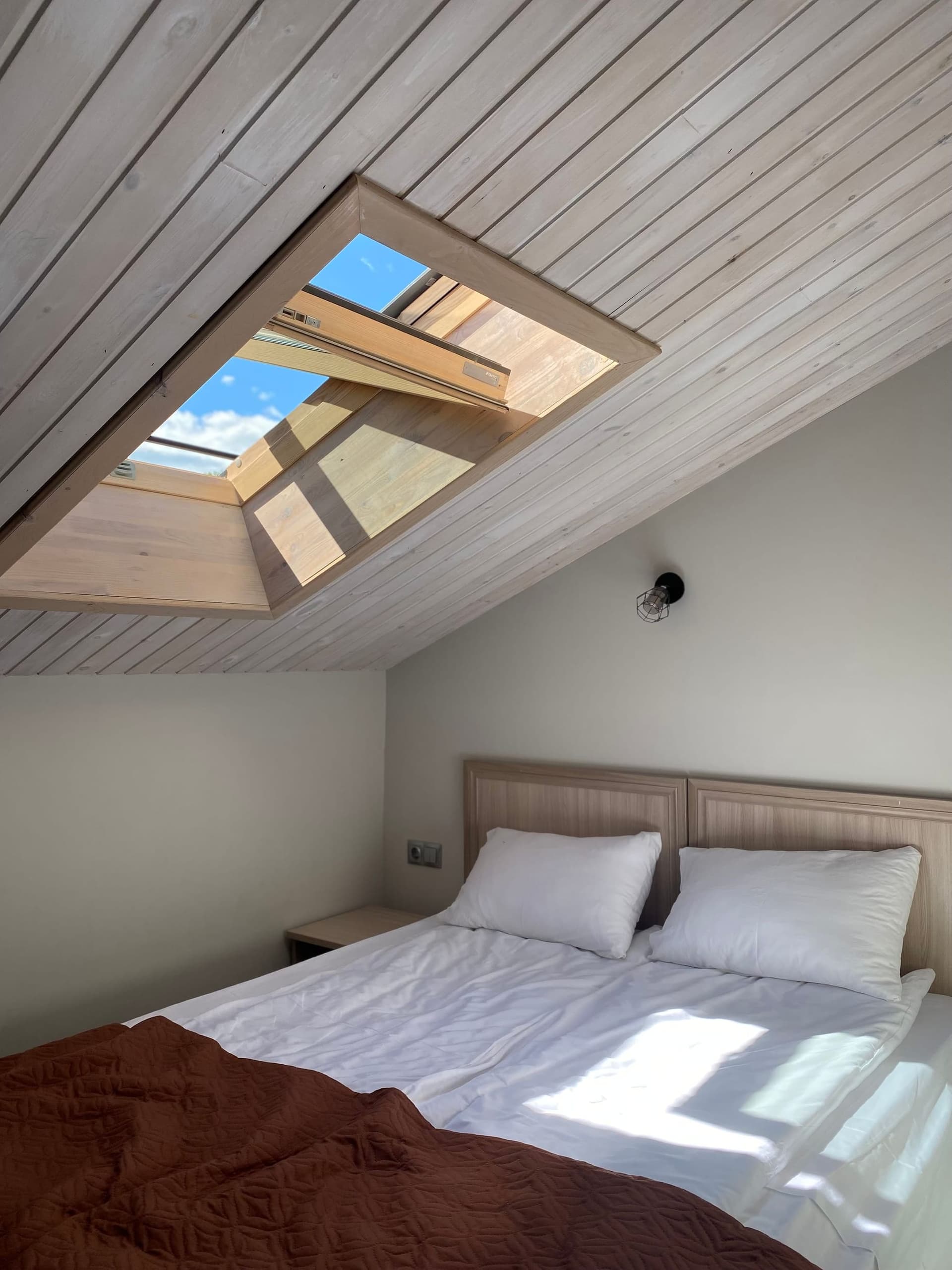 Double bed beneath a rooflight set into a sloping timber-clad ceiling